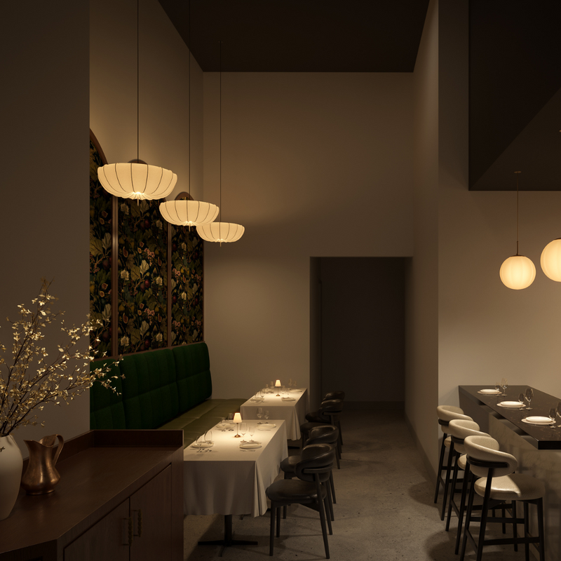 A modern, dimly lit restaurant interior with hanging pendant lights, a green upholstered booth, a bar counter with stools, and shelves of bottles on the right.